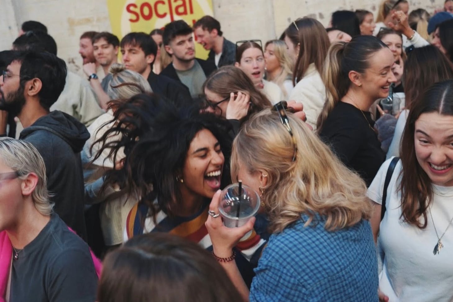 An image of two girls in a club crowd who are dancing and singing happily while facing each other.